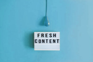 Lightbox with the words fresh content on it sitting on a blue background with a blue lightbulb hanging over it